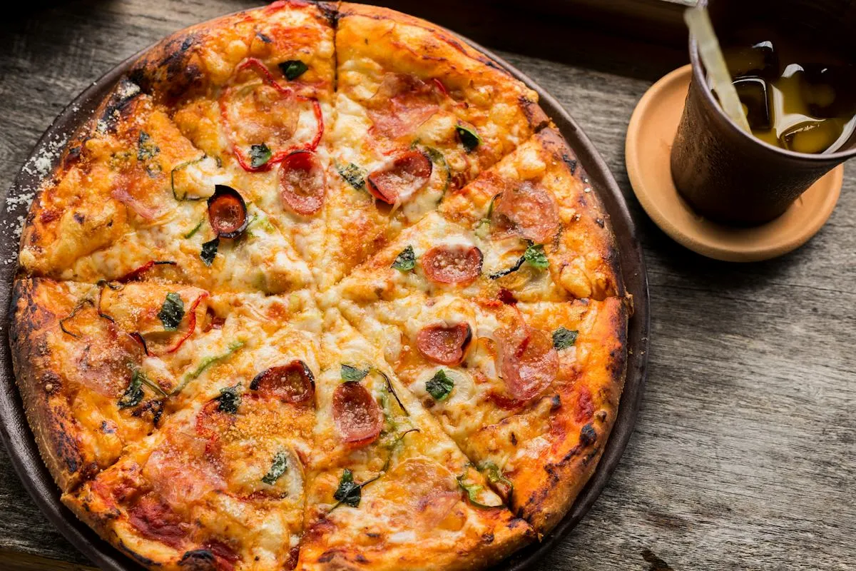 Baked pizza covered in cheese and seasonal toppings on a timber table